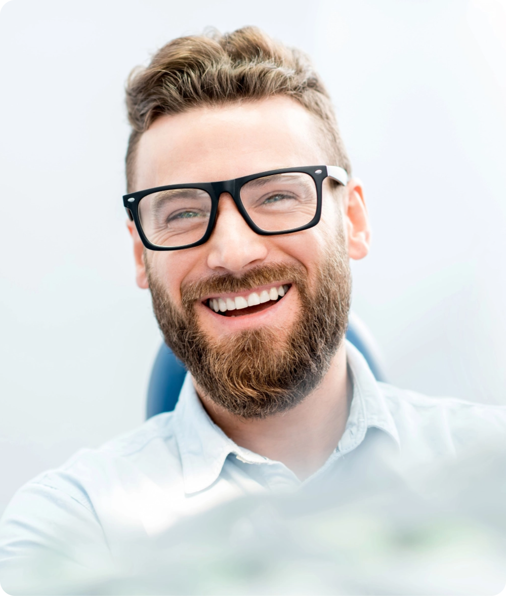 Smiling man with glasses and beard in dental clinic chair